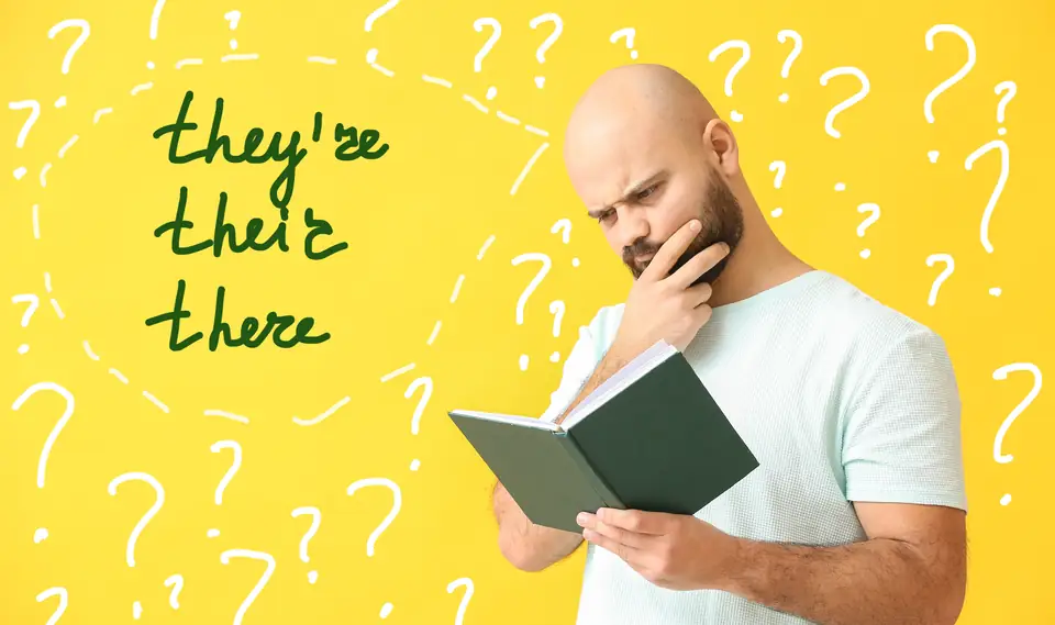 A man reading a book beside the words they’re, their and there on a yellow background.
